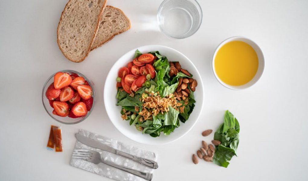 Top view of a healthy salad and fresh ingredients with bread and juice on a white surface.